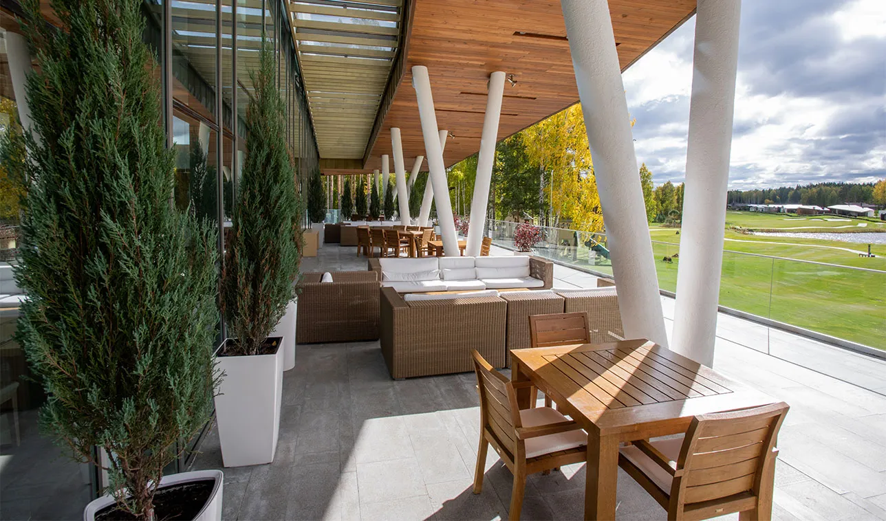 Wooden table, chairs and couches outdoors along large windows